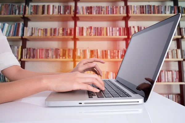 Mão mulher usando laptop na mesa branca com backgroun prateleira do livro — Fotografia de Stock