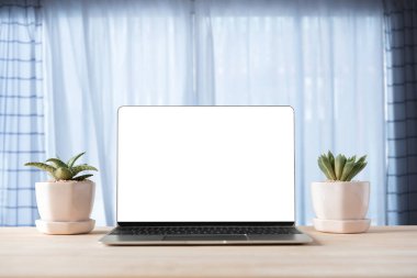 Ahşap masa ve pencere zemininde boş beyaz ekran olan dizüstü bilgisayar
