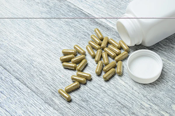 Herbal Pills spilling from Bottle on wooden table background — Stock Photo, Image