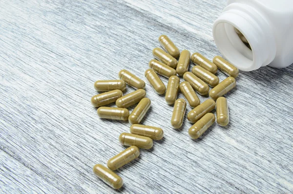 Herbal Pills spilling from Bottle on wooden table background — Stock Photo, Image