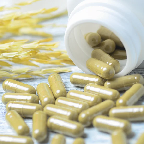 Växtbaserade piller rinner från flaska på träbord bakgrund — Stockfoto