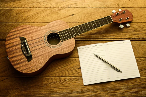 Guitarra ukulele com caderno e lápis em branco — Fotografia de Stock