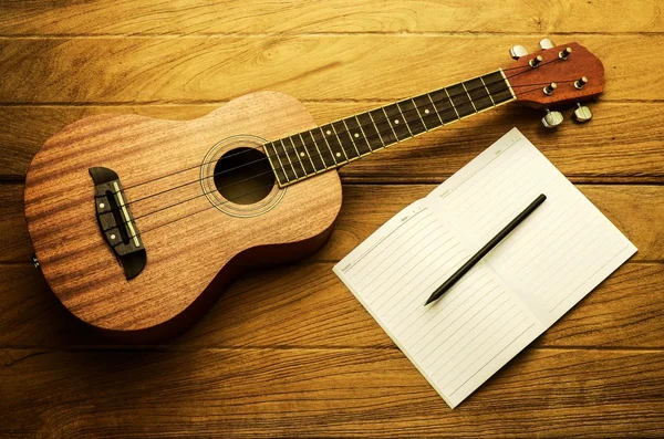 Guitarra ukelele vintage y nota de canción en mesa de madera —  Fotos de Stock