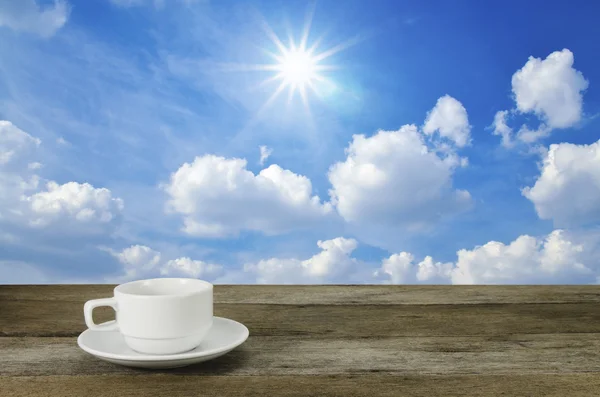 Taza de café sobre mesa de madera con cielo azul y fondo de sol —  Fotos de Stock