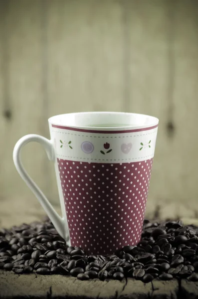 Xícara de café na mesa de madeira e grãos de café torrados ao redor — Fotografia de Stock