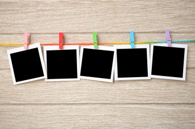 empty black photo frames hanging with clothespins on wooden back clipart