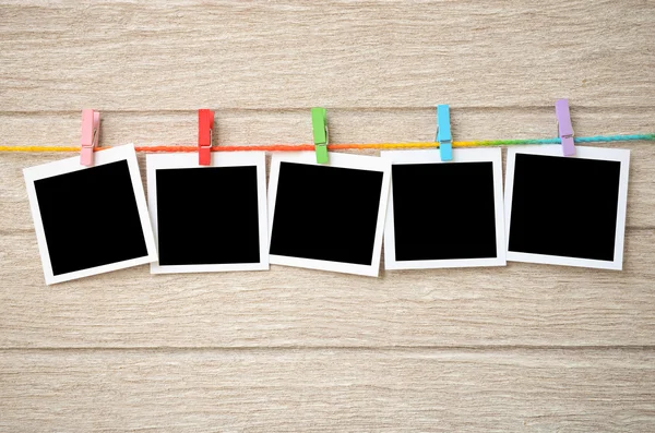 Empty black photo frames hanging with clothespins on wooden back — Stock Photo, Image