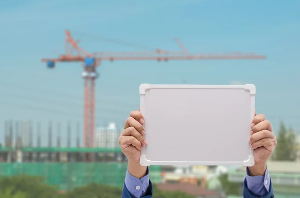 Hombre de negocios mano sosteniendo pizarra blanca con fondo de obra —  Fotos de Stock