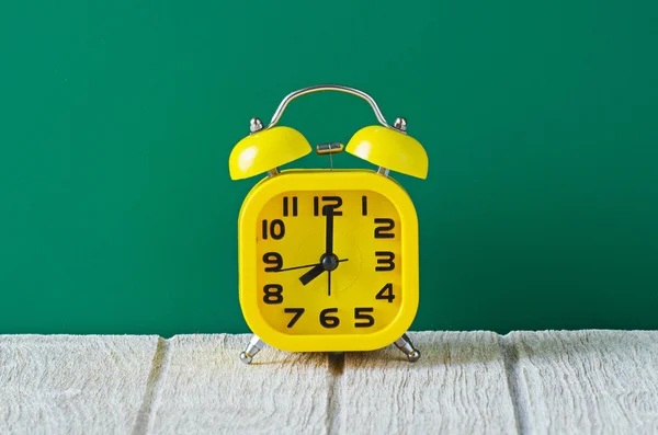 Reloj despertador amarillo sobre mesa de madera con fondo verde —  Fotos de Stock