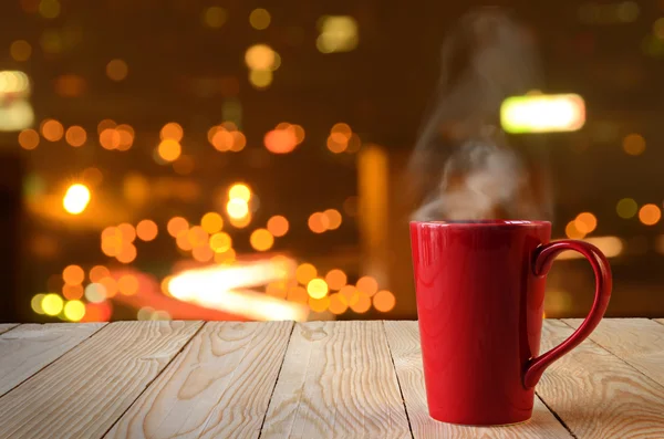 Tasse de café rouge avec fumée sur fond bokeh de la ville — Photo