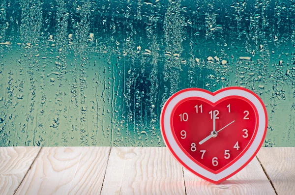 물방울 유리 창 배경으로 나무 테이블에 빨간 시계 — 스톡 사진
