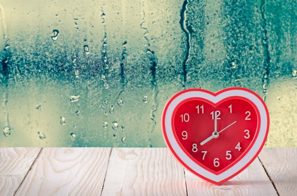 Reloj rojo sobre mesa de madera con gotita de agua sobre fondo de ventana de cristal —  Fotos de Stock