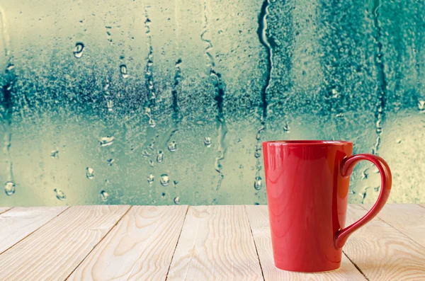 Rode koffiekopje met natuurlijke water druppels op glazen venster achtergrond — Stockfoto