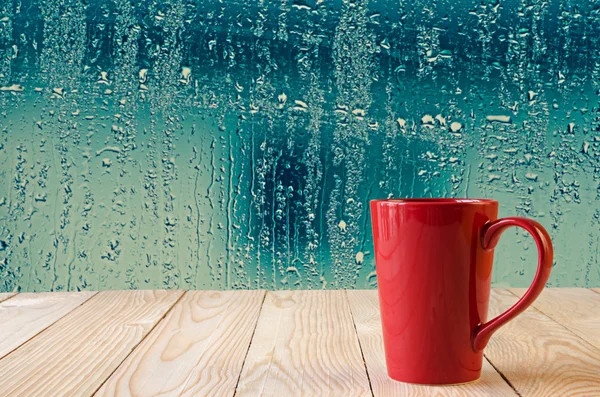 Rode koffiekopje met natuurlijke water druppels op glazen venster achtergrond — Stockfoto