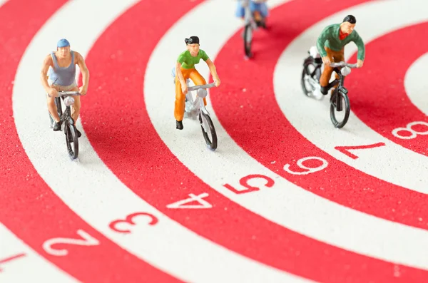 Miniature people cycling on darts — Stock Photo, Image