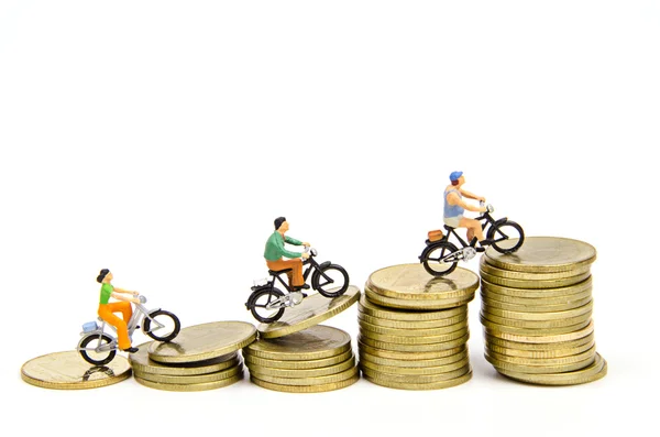 Miniature people ride on stack of coins — Stock Photo, Image