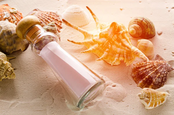 Fles brief en zee schelpen op zand achtergrond — Stockfoto