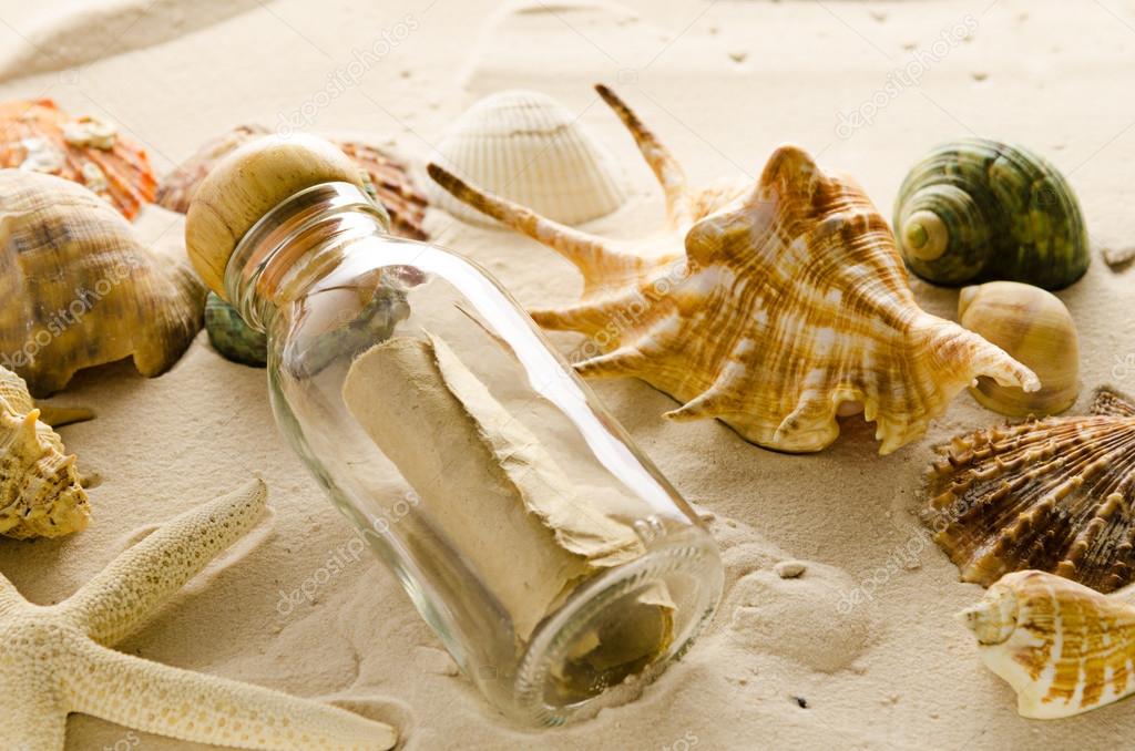 bottle letter and sea shells on sand background