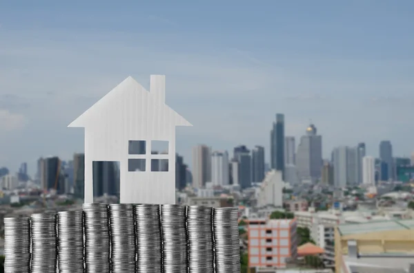 Modelo de casa en pila de moneda con fondo borroso de la ciudad moderna —  Fotos de Stock