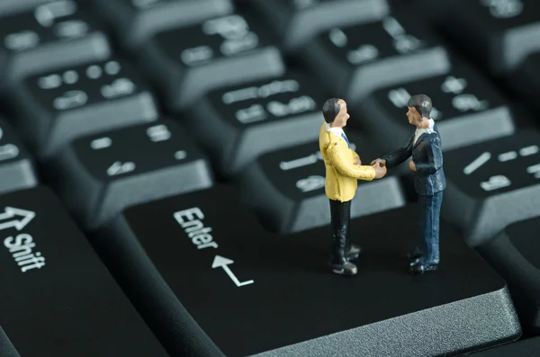 Miniaturmenschen geben sich auf Tastatur-Hintergrund die Hand — Stockfoto