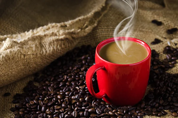 Taza de café con humo y granos de café alrededor — Foto de Stock