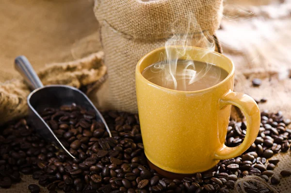 Xícara de café com fumaça e grãos de café ao redor — Fotografia de Stock