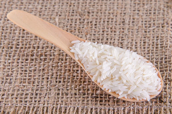 Uncooked rice in wooden spoon on sack background — Stock Photo, Image