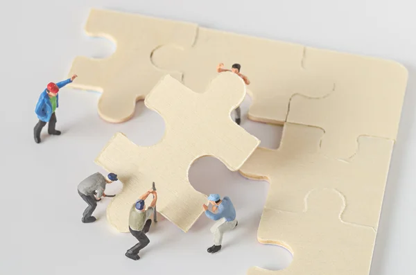 Miniaturowe pracownik zespołu spróbuj ukończyć puzzle układanki — Zdjęcie stockowe