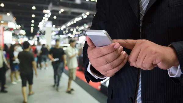 Uomo d'affari utilizzando il telefono cellulare con sfondo evento sfocato — Foto Stock