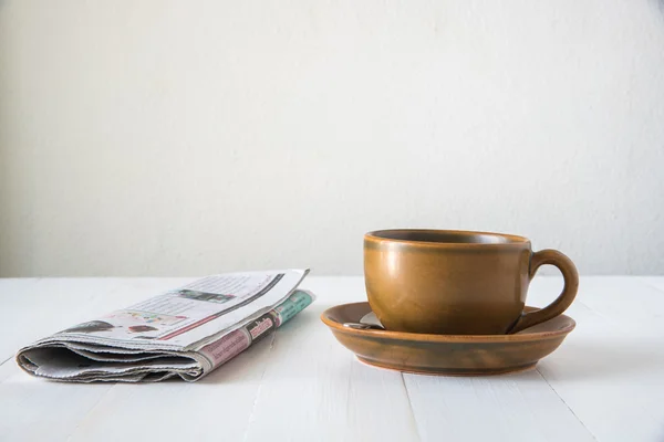 Bruin koffiekopje en krant op witte houten tafel — Stockfoto