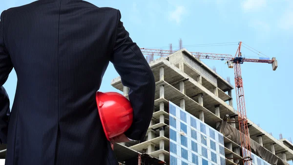 Homem de negócios segurando capacete de segurança vermelho com local de construção ba — Fotografia de Stock