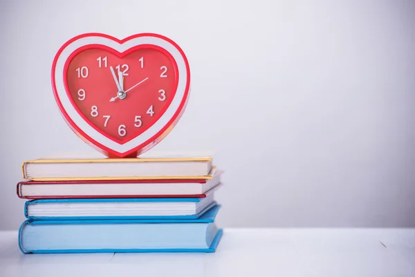 Κόκκινη καρδιά ρολόι και στοίβα του βιβλίου στο ξύλινο τραπέζι — Φωτογραφία Αρχείου