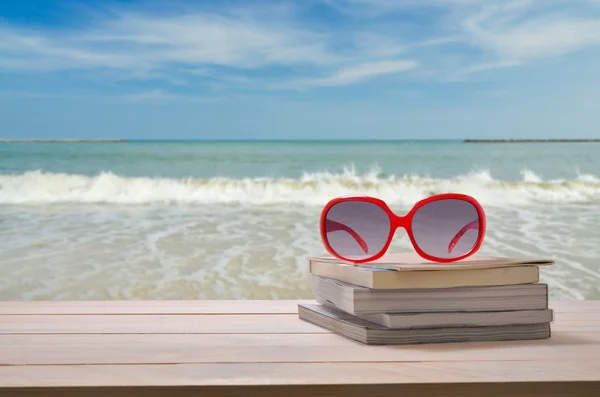 海背景を持つ本のスタックの赤いサングラス — ストック写真
