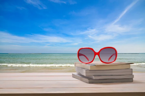 海の景色の背景が付いている本のスタックの赤いサングラス — ストック写真