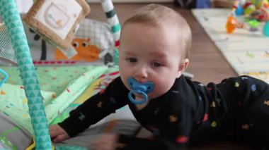 Oyun sırasında hafif bir çocuk konforu. Sakinleştirici Emziği Olan Sakin Bebek, Kapalı Kapılar Arasındaki Şefkatli İlişki 'nin tadını çıkarıyor. Bebek, oyun sırasında huzur içinde, emzik ve huzur dolu bir ifadeyle canlı bir Mat 'ın üzerinde yatıyor.