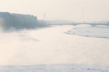 Neva Nehri 'nin üzerinde gün batımıyla birlikte güzel mistik bir kış manzarası. Suyun üstünde buhar, ufukta karla kaplı bir buz ve ufukta sisli bir köprü. Rusya' daki St. Petersburg şehri manzarası.
