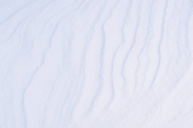 Karların yakın çekim şekli, buz kristallerinden yapılmış temiz beyaz kar dokusu, tahıllı bir yüzeyde, soğuk kış rüzgarından gelen soyut bir desen, çöldeki kum tepesi gibi, arka planda.