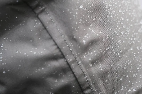 湿淋淋的雨衣 由光滑而紧密的灰色防水织物制成 雨滴图案涂在厚重的纺织材料上 水滴在浓密而光亮的灰色表面 水滴滴在粗糙的布上 — 图库照片