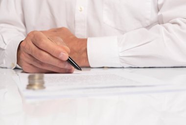 Sözleşme imzalama konsepti. İşadamı elinde kalemle belgeyi kapatıyor. para ön planda bulanıklaştırıldı