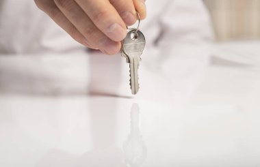 Kravatlı bir işadamının eli, beyaz masanın üzerinde duran ve yansıması olan yeni bir daireden anahtar veriyor..