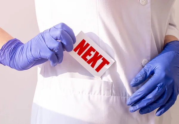 Next word on paper in doctor hands in blue protective gloves in white uniform close up, medical concept