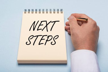 Sarı defterdeki bir sonraki adım, mavi masadaki erkek eli, üst görünüm.