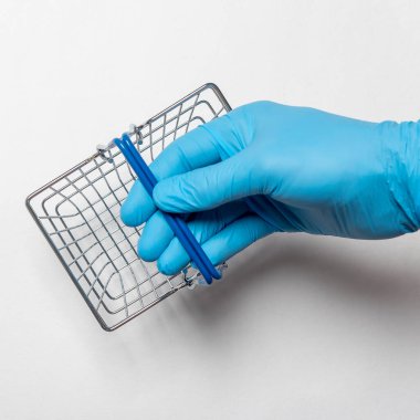 Erkek eli mavi koruyucu eldivenli boş metal bir sepet. Beyaz arka planda izole edilmiş Coronavirus kilitleme konsepti sırasında alışveriş