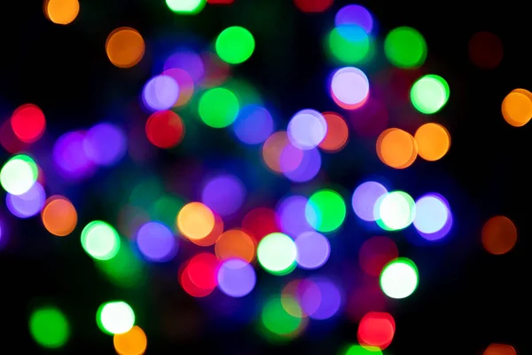 Blurred multicolored christmas lights on black background. Xmas backdrop for design or printing. New year texture.