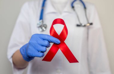 Red ribbon for aids world day support, close up of doctor hand in glove.