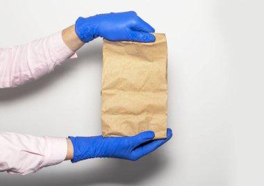 Güvenli teslimat konsepti. Beyaz arka planda koruyucu eldivenlerle kuryenin elinde bir paket ya da el işi. Güvenli internet alışverişi.