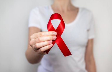 AIDS ve HIV dünya desteği için kırmızı kurdele, yakın çekim. Arka planda beyazlar içindeki bulanık kadın.
