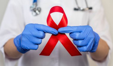 AIDS ve HIV dünya desteği için kırmızı kurdele, yakın çekim. Kadın doktorun eli..
