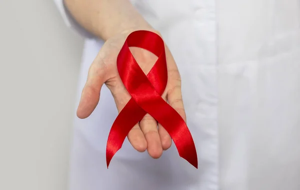 Red ribbon for aids and hiv world day support, close up. Hand of female doctor.