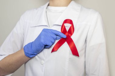 AIDS ve HIV dünya desteği için kırmızı kurdele, yakın çekim. Kadın doktorun eli..